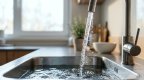 Wasserstrahl aus einem modernen Armaturenhahn im Gegenlicht