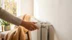 Hand stellt ein Thermostatventil an einem Heizkörper ein